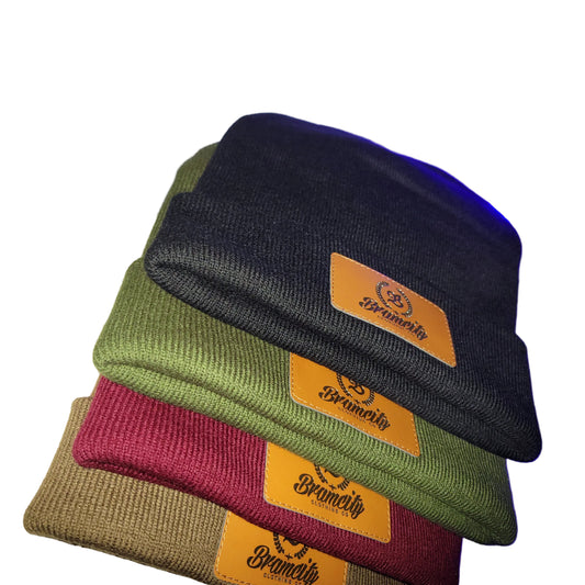 Four beanies in black, green, red, and brown with a brand logo on a textured surface.